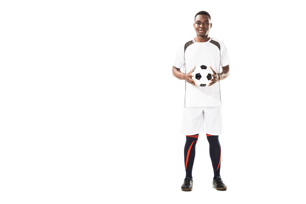 Вид в полный рост счастливого молодого африканского футболиста, держащего мяч и улыбающегося камере на белом фоне
 - Фото, изображение