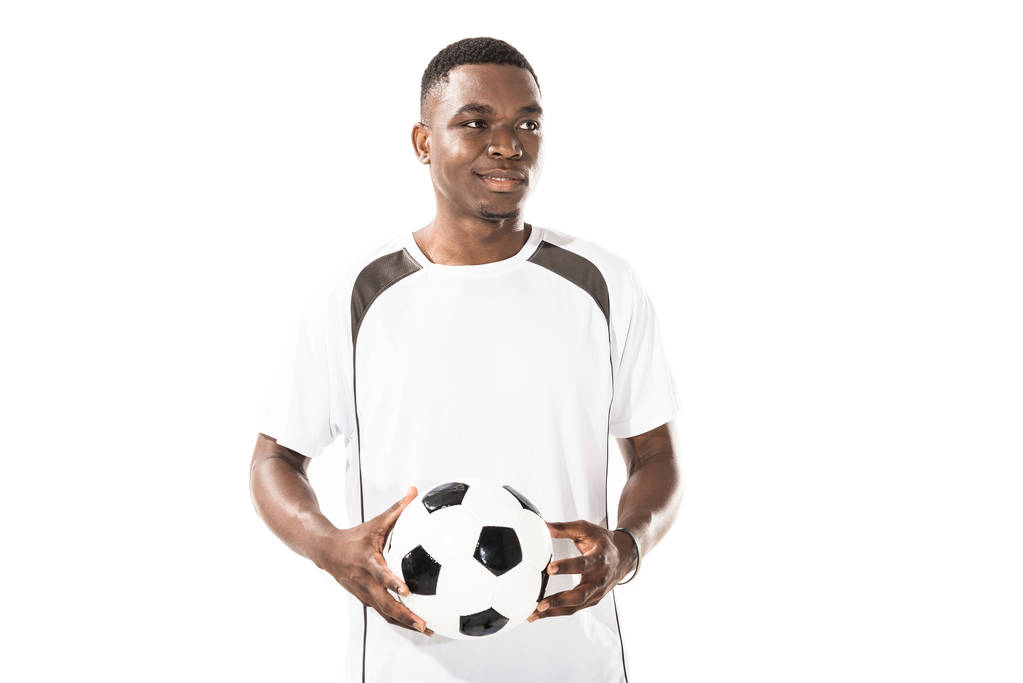 lachende jonge Afro-Amerikaanse sportman holding voetbal en op zoek weg geïsoleerd op wit - Foto, afbeelding