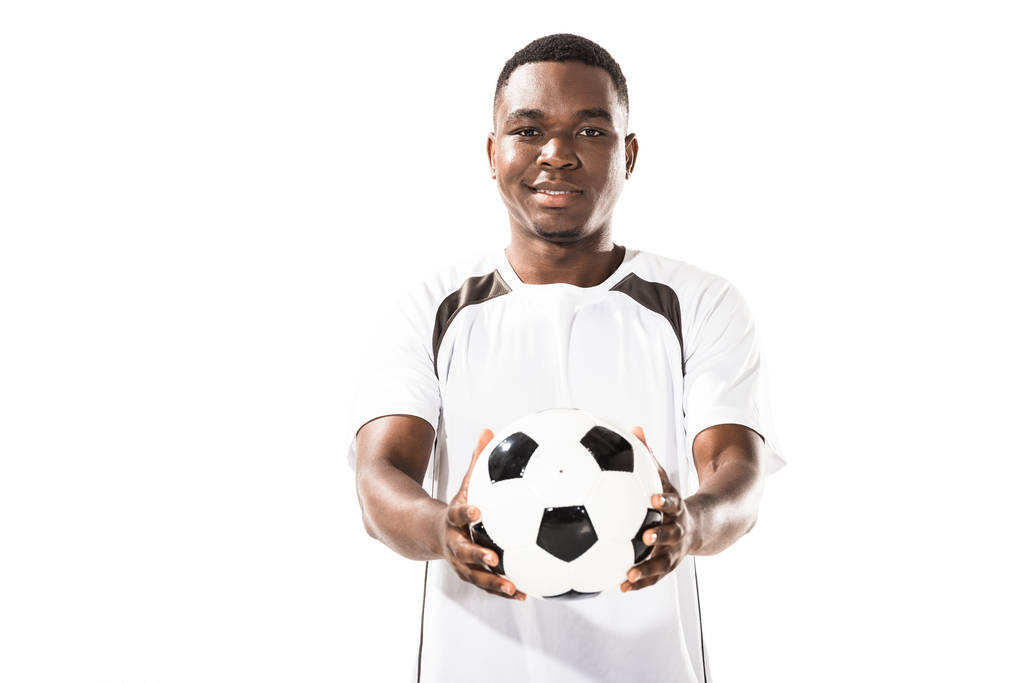 guapo feliz joven afroamericano deportista sosteniendo pelota de fútbol y sonriendo a la cámara aislado en blanco
 - Foto, imagen