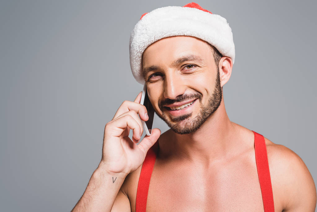portret szczęśliwy muskularny mężczyzna w Boże Narodzenie kapelusz mówić na smartphone na białym tle na szarym tle - Zdjęcie, obraz