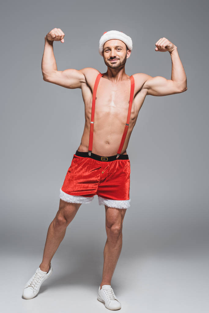 giovane uomo muscoloso in cappello di Natale mostrando muscoli isolati su sfondo grigio
 - Foto, immagini