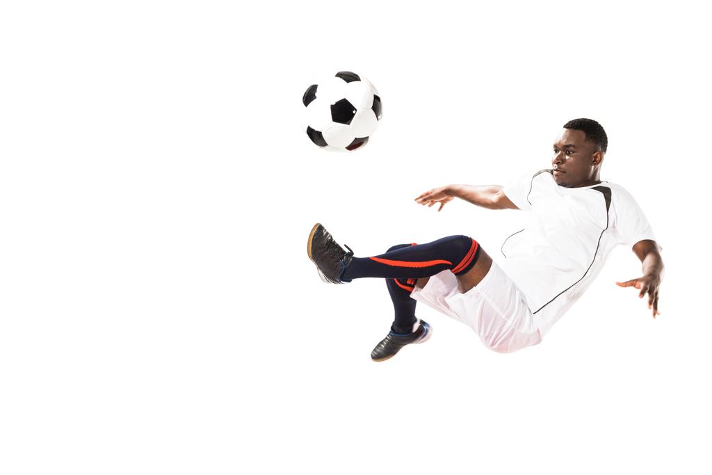 αθλητική νεαρός αφρικανική αμερικανική ποδοσφαιριστής κλωτσάει την μπάλα στο άλμα που απομονώνονται σε λευκό  - Φωτογραφία, εικόνα
