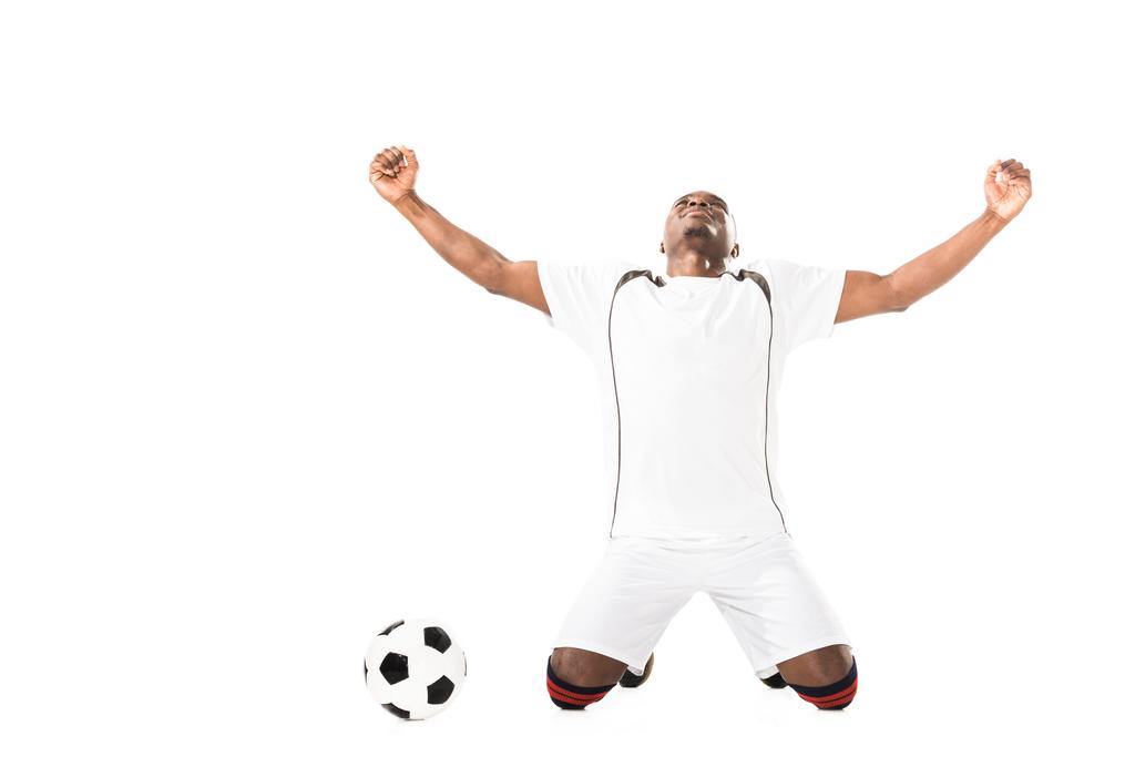 θριαμβεύοντας νεαρός αφρικανική αμερικανική ποδοσφαιριστής γονατιστή κοντά μπάλα που απομονώνονται σε λευκό  - Φωτογραφία, εικόνα