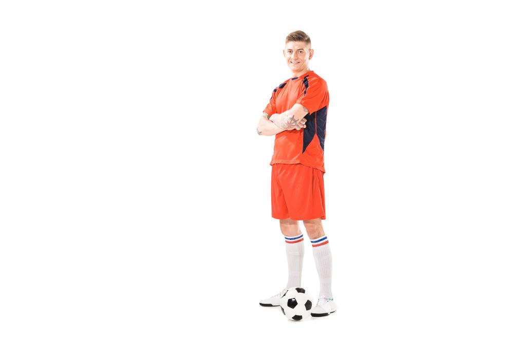 πλήρες μήκος προβολής αθλητικό νεαρό ποδοσφαιριστή στέκεται με σταυρωμένα χέρια και να χαμογελά στη φωτογραφική μηχανή που απομονώνονται σε λευκό - Φωτογραφία, εικόνα
