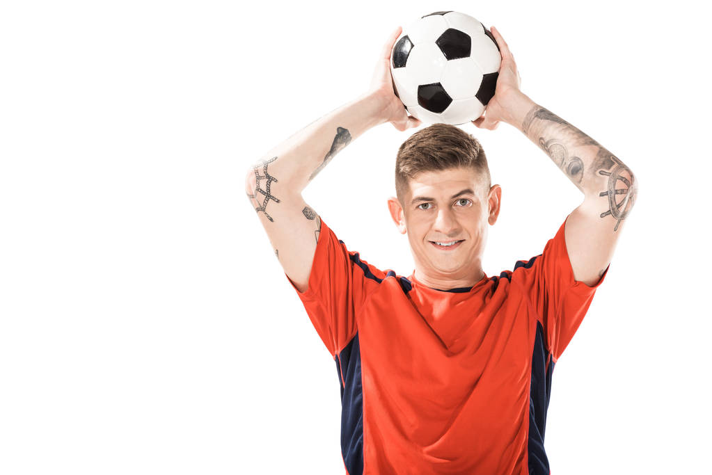 schöner junger Sportler, der einen Fußballball über dem Kopf hält und isoliert in die Kamera lächelt - Foto, Bild