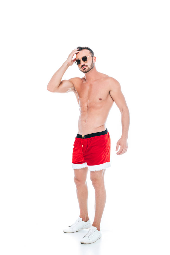 homme musclé torse nu en lunettes de soleil et short Père Noël debout isolé sur fond blanc
  - Photo, image