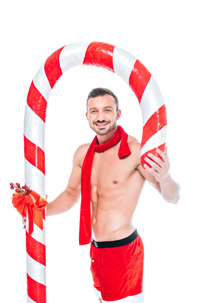homme musclé torse nu heureux en short Père Noël et écharpe rouge avec bâton de Noël rayé isolé sur fond blanc
 - Photo, image