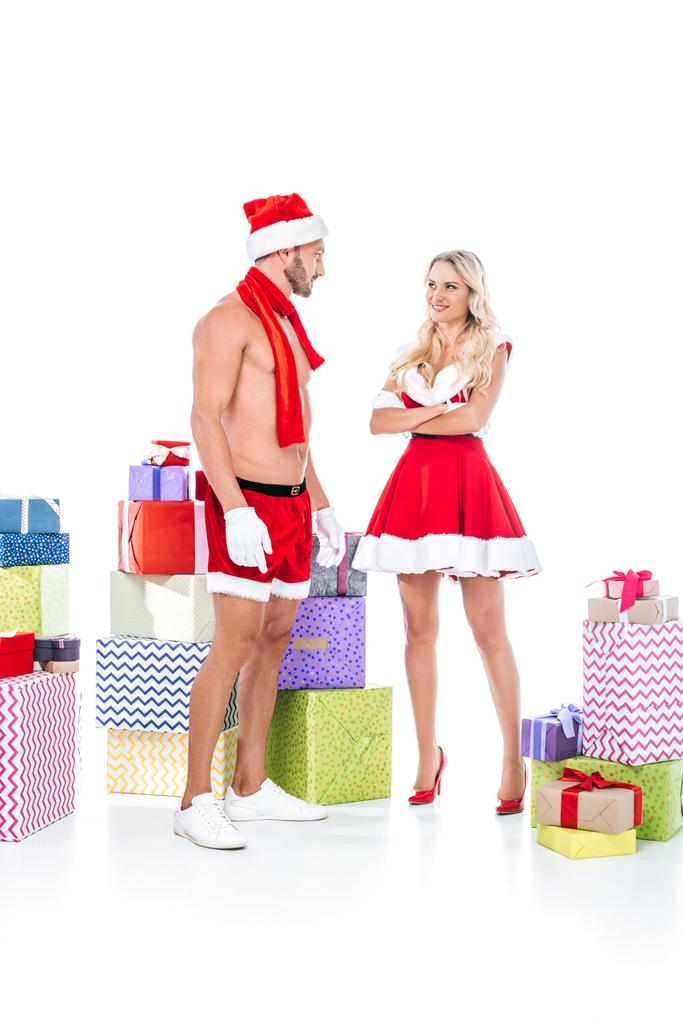 feliz pareja joven en ropa de Navidad de pie cerca de la pila de cajas de regalo aislados sobre fondo blanco
 - Foto, Imagen