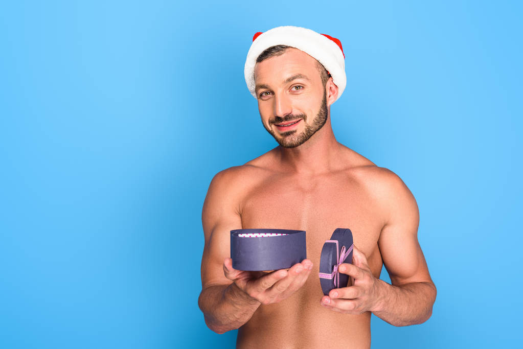 portrait de l'homme musclé torse nu dans le chapeau de Noël tenant boîte cadeau isolé sur fond bleu
 - Photo, image