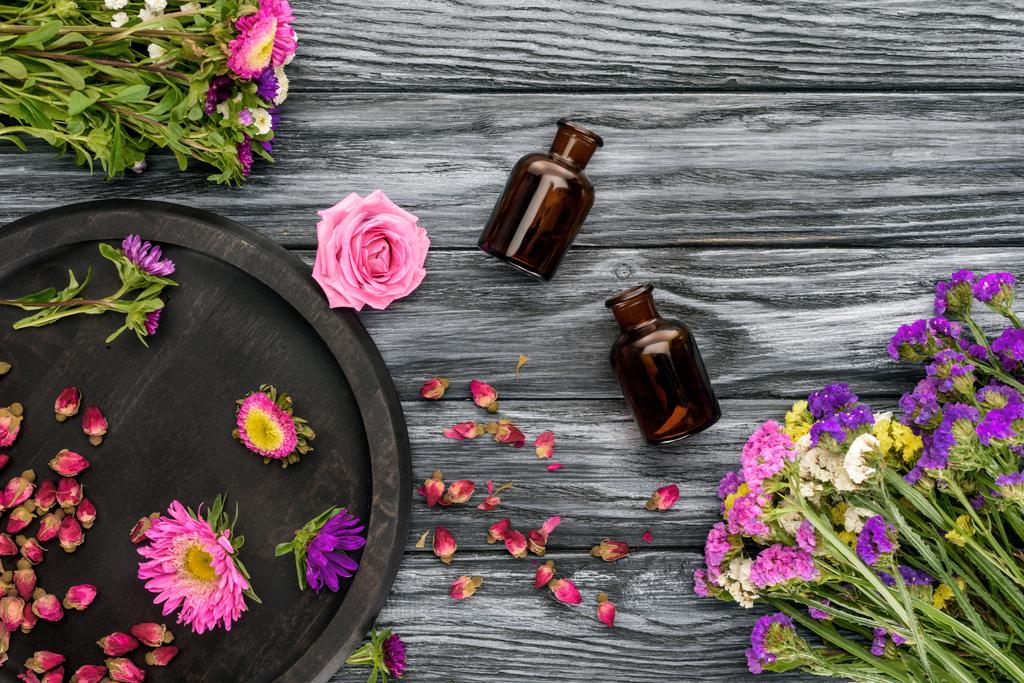 το Top view από μπουκάλια φυσικά φυτικά αιθέρια έλαια και ροζ με μοβ άνθη σε ξύλινη επιφάνεια - Φωτογραφία, εικόνα
