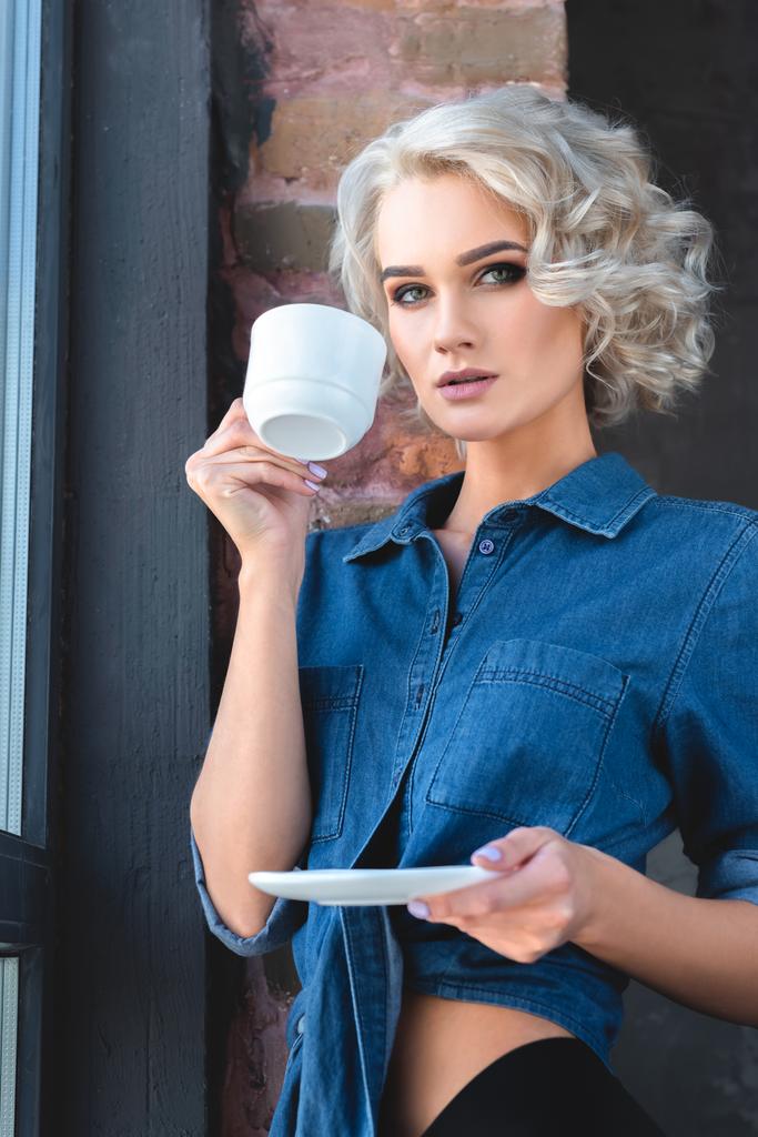 attrayant jeune femme en denim chemise boire du café et regarder la caméra
 - Photo, image