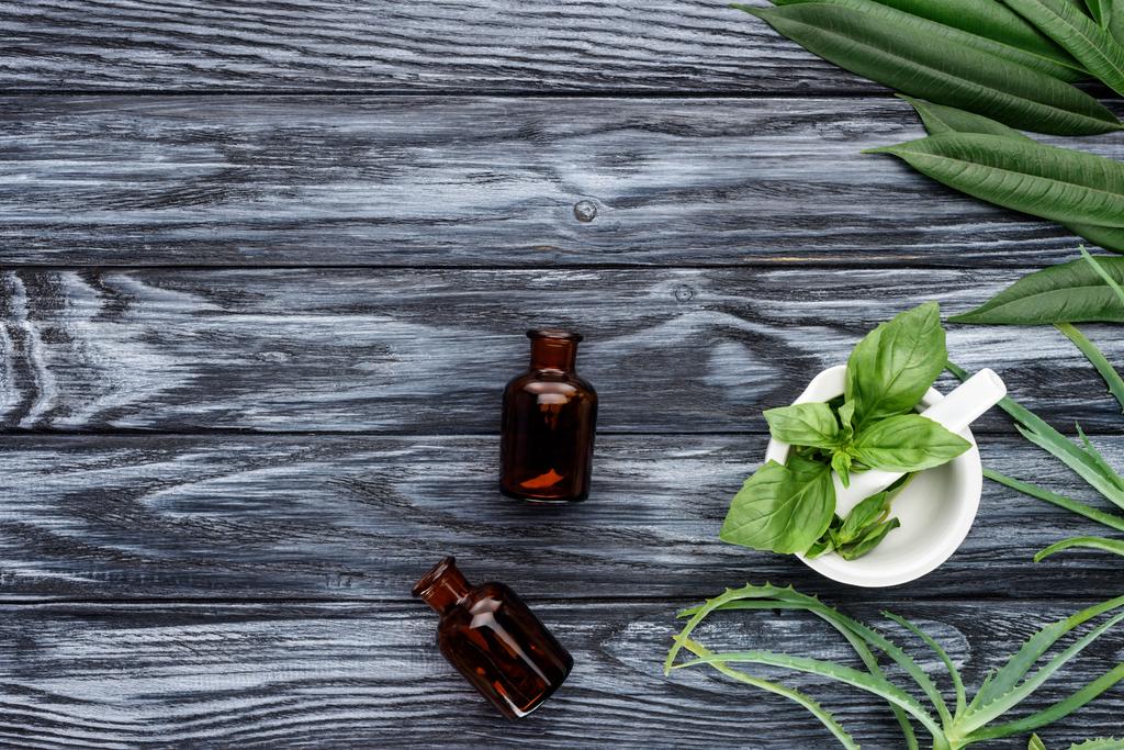 top view of two bottles of natural herbal essential oils and green herbs on wooden table - Photo, Image