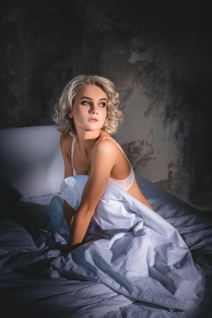 atrakcyjna młoda kobieta w bieliźnie, siedząc na łóżku pod zachód słońca promienie i szukasz drogi - Zdjęcie, obraz
