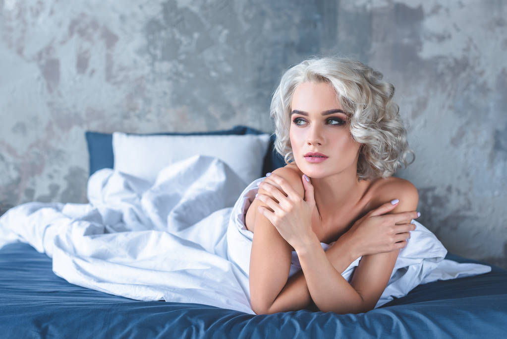 seductora joven sentada en la cama cubierta con manta blanca
 - Foto, imagen