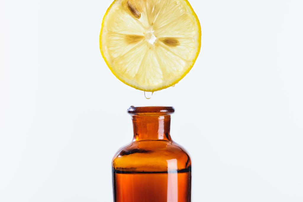doğal bitkisel uçucu yağ üzerinde beyaz izole şişe içine damlayan limon parçanın aromatik meyve suyu - Fotoğraf, Görsel