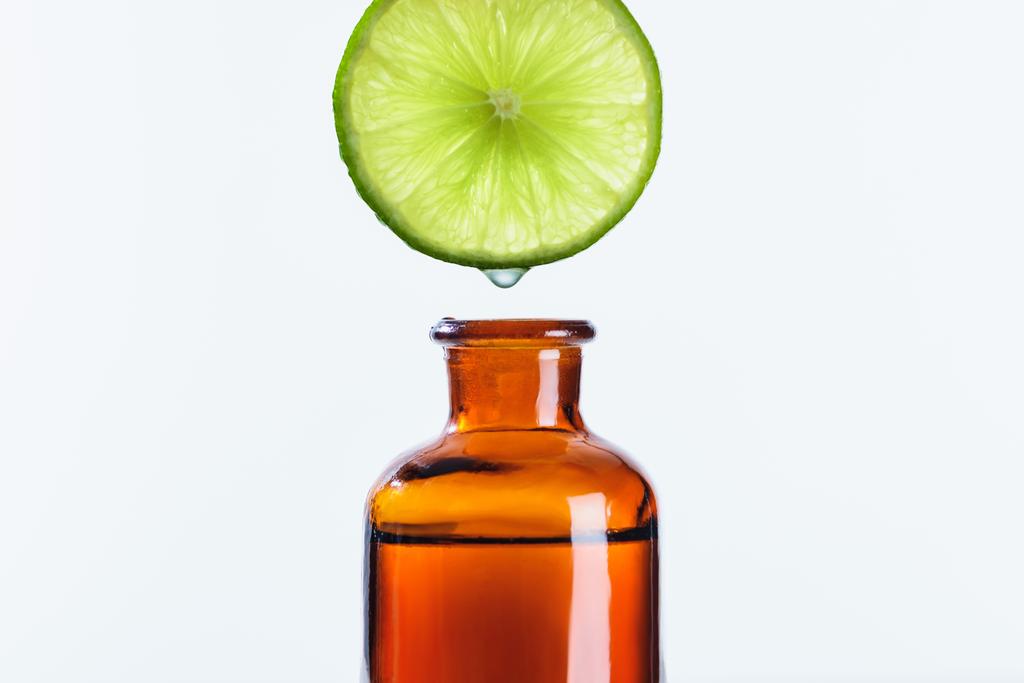 aromatischer Saft aus Limettenstücken, der in eine Flasche mit natürlichem ätherischem Kräuteröl tropft, isoliert auf weiß - Foto, Bild