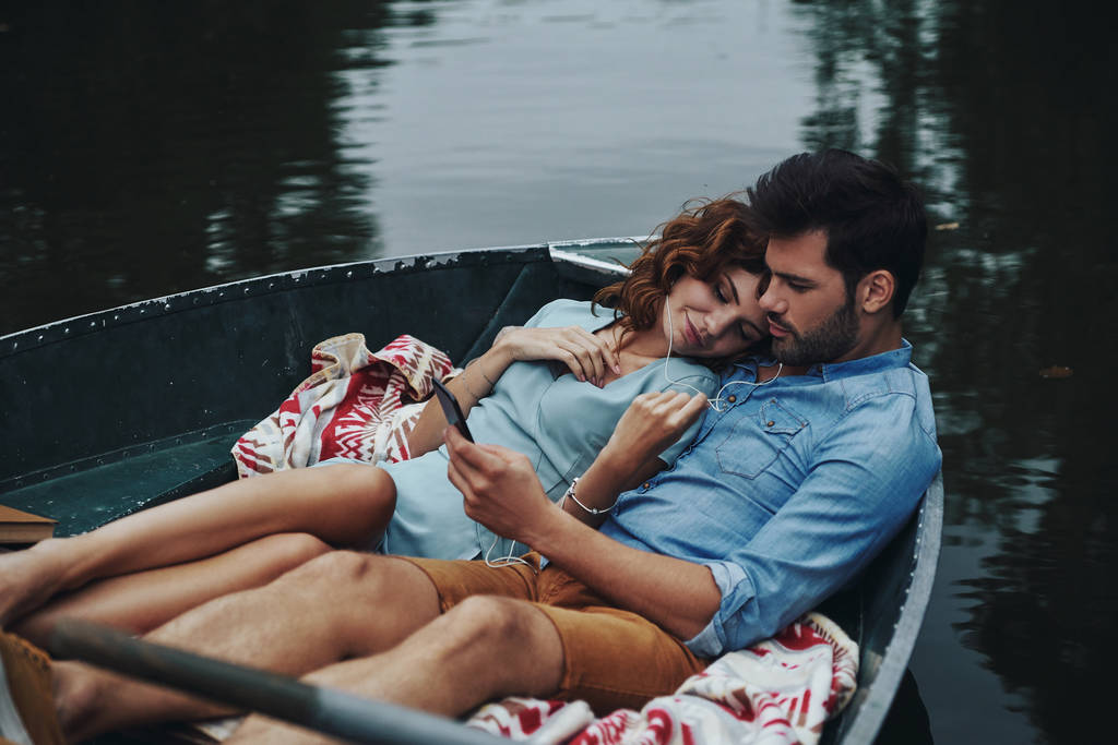 Deux cœurs pleins d'amour. Beau jeune couple écoutant de la musique assis dans le bateau à l'extérieur
 - Photo, image