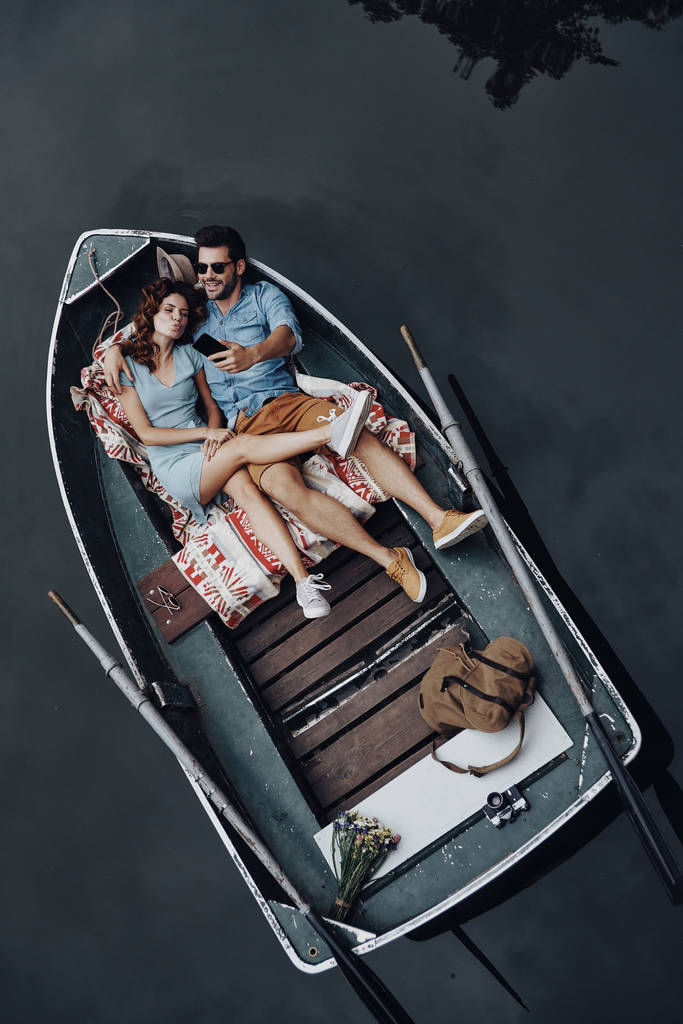 美しいカップル彼氏とボートで横になっている携帯電話のトップ ビュー - 写真・画像