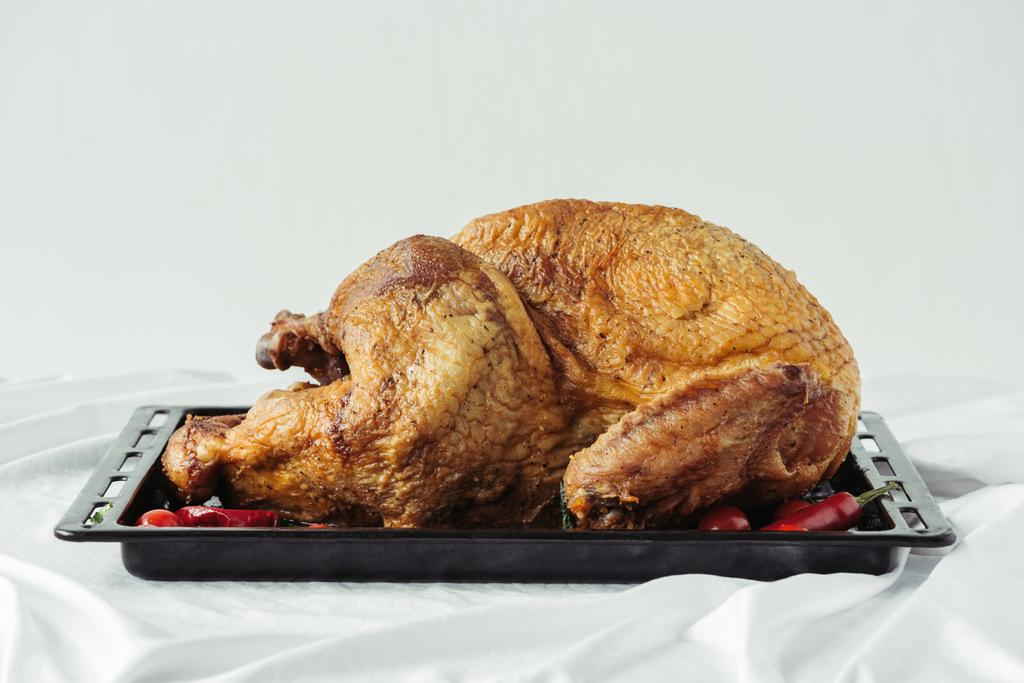 Close-up van gekookte feestelijke Turkije op bakselpan op oppervlak met tafelkleed op grijze achtergrond, diner concept thanksgiving vakantie - Foto, afbeelding