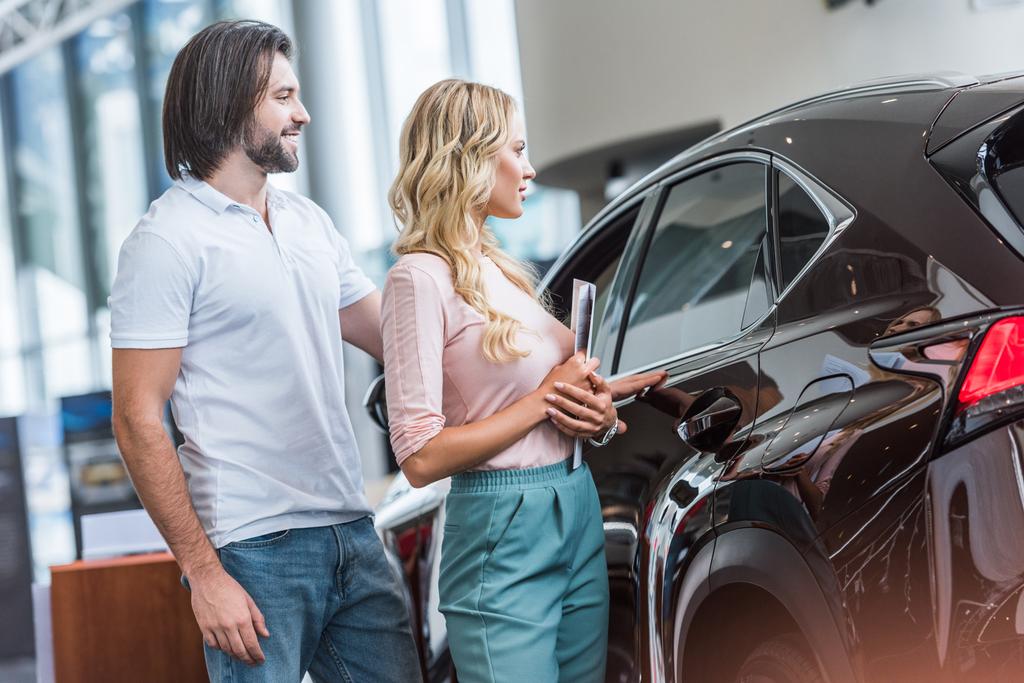 ζευγάρι με κατάλογο που αγοράζουν αυτοκίνητο σε αντιπροσωπεία σαλόνι - Φωτογραφία, εικόνα