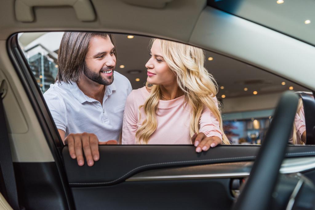 pareja joven de pie en el nuevo automóvil en el salón de concesionarios
 - Foto, imagen