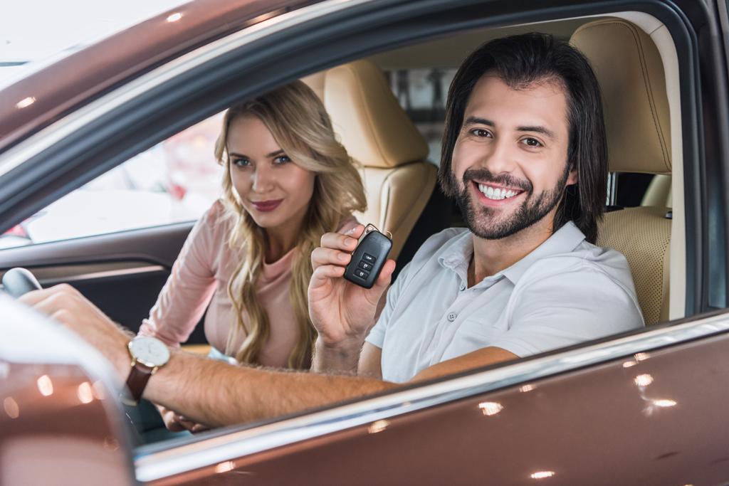 smiling couple with car key sitting in new car at dealership salon - Photo, Image