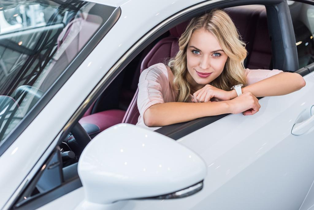 portrét mladé ženy, zatímco sedí v novém autě v autorizovaném salonu při pohledu na fotoaparát - Fotografie, Obrázek