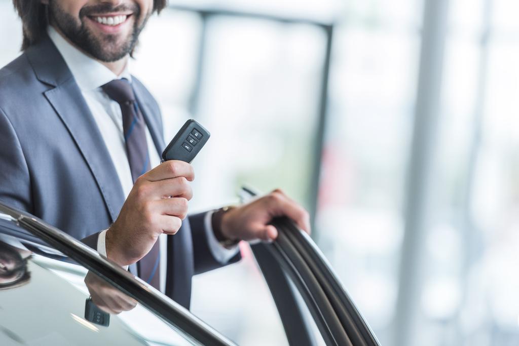 обрізаний знімок усміхненого бізнесмена з ключем від машини, що стоїть в новому автомобілі в дилерському салоні
 - Фото, зображення