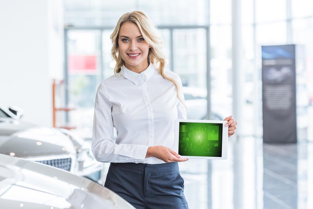 portrait of smiling seller showing tablet with graphic diagram in hands in dealership salon - Photo, Image