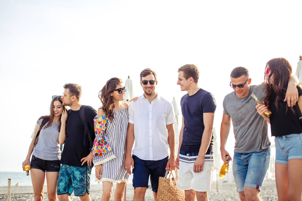 праздники, каникулы. группа друзей, развлекающихся на пляже, гуляющих, пьющих пиво, улыбающихся и обнимающихся - Фото, изображение
