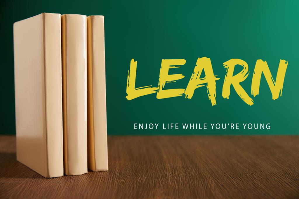 three books on wooden table with chalkboard on background with "learn - enjoy life while you are young" lettering - Photo, Image
