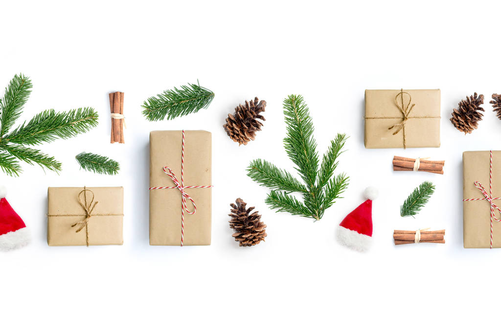 Gelukkig Kerstmis lay-out samenstelling, bovenaanzicht met xmas presenteert, kaneelstokjes, fir boomtakken en dennenappels op een witte achtergrond. - Foto, afbeelding