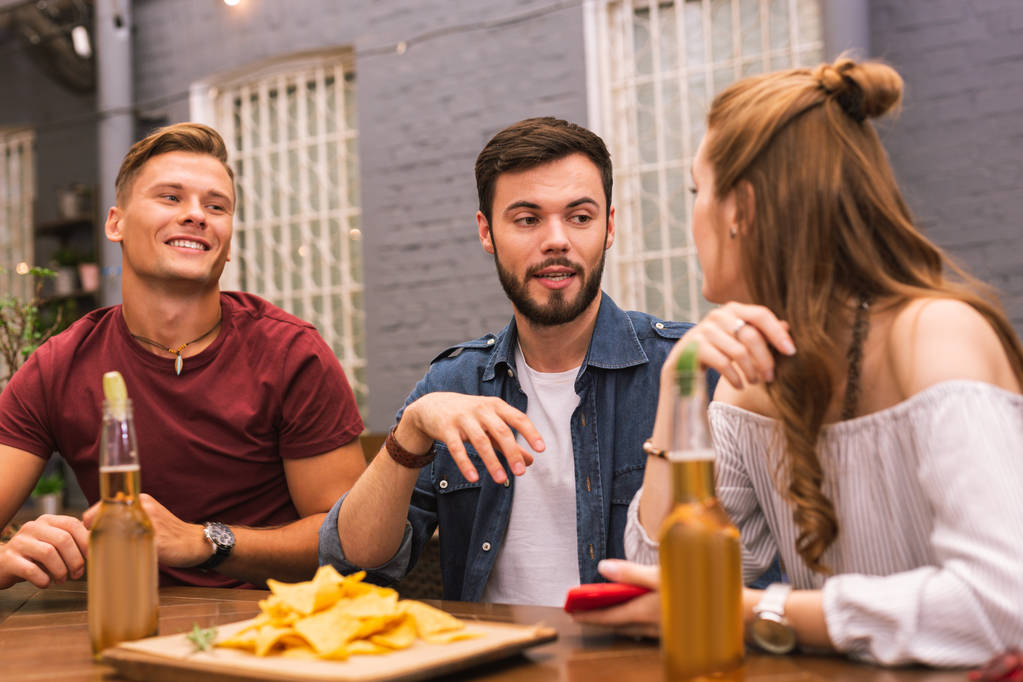 Троє молодих людей розмовляють і їдять у барі
 - Фото, зображення