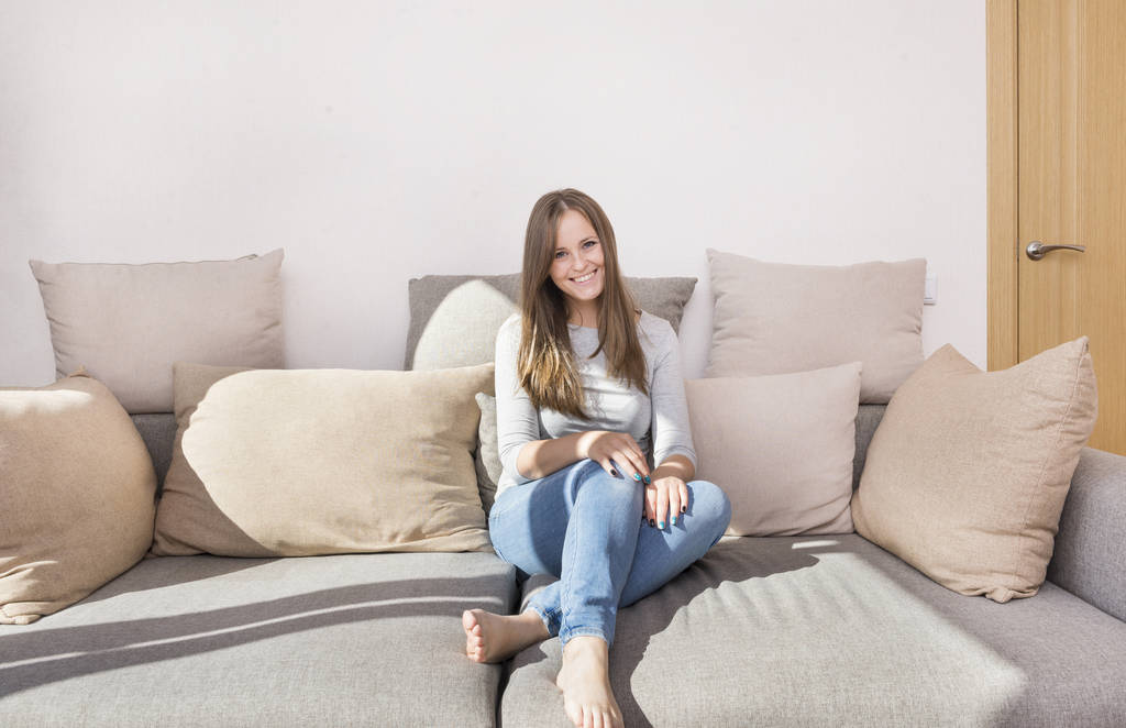 uma menina branca com cabelos longos em jeans sentado no sofá, 1 jovem sorrindo, emoções
 - Foto, Imagem