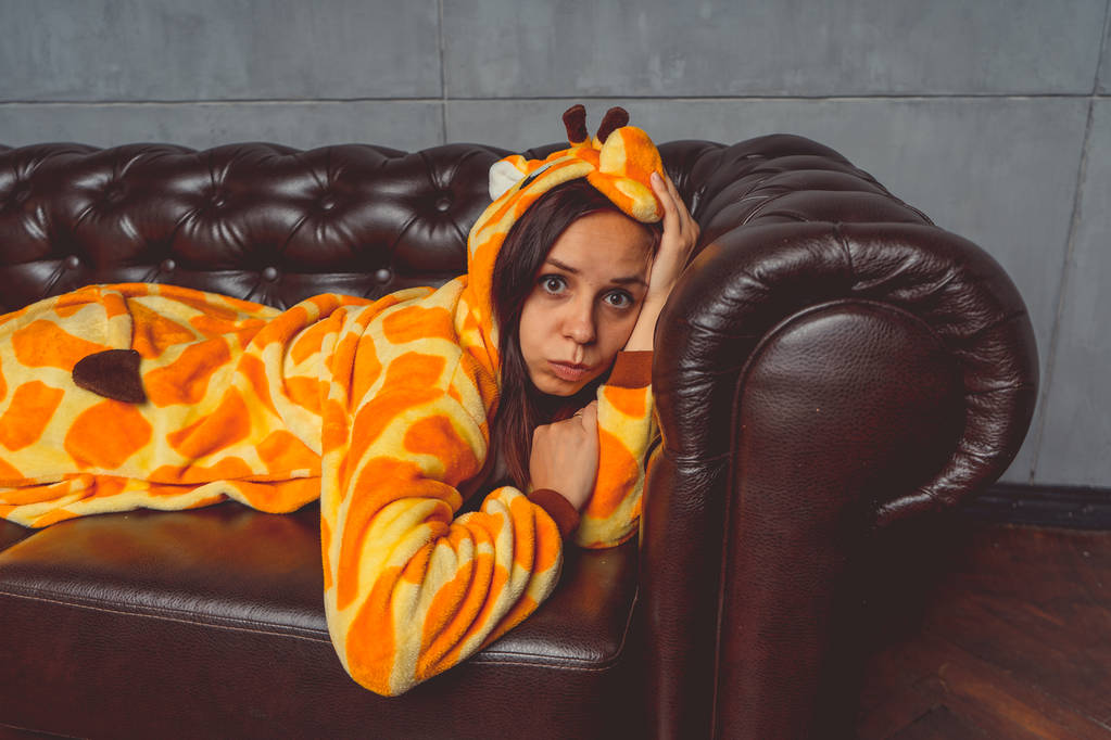 Pajamas in the form of a giraffe. Emotional portrait of a student on the background leather sofa. Crazy and funny man in the suit. - Photo, Image