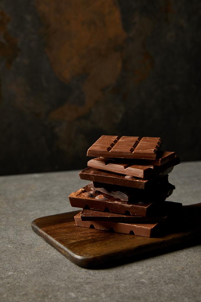 νόστιμα ανάμικτες κομμάτια σοκολάτας σε ξύλινη σανίδα σε γκρι  - Φωτογραφία, εικόνα