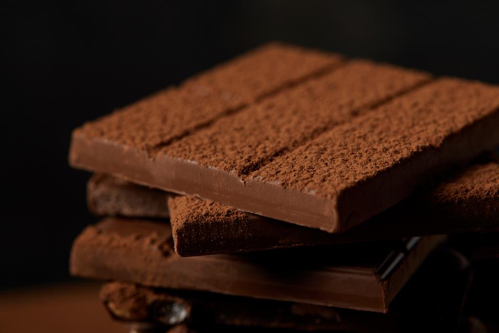 vista de cerca de deliciosas barras de chocolate surtidos con cacao en polvo en negro
 - Foto, imagen