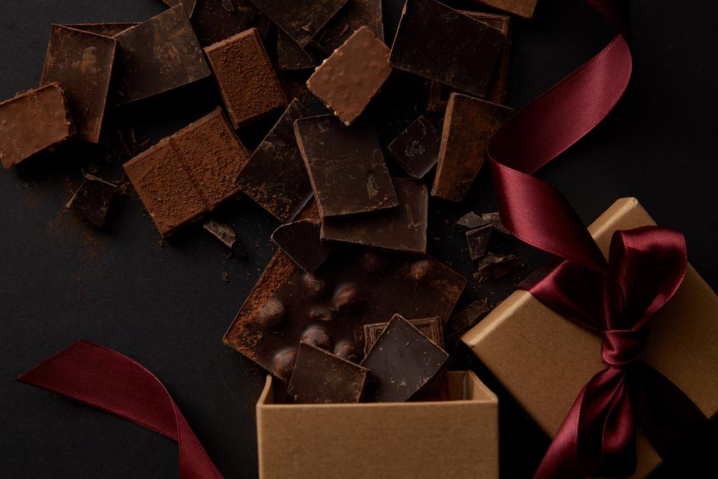 вид зверху на подарункові коробки та смачні шоколадні шматочки на чорному
 - Фото, зображення