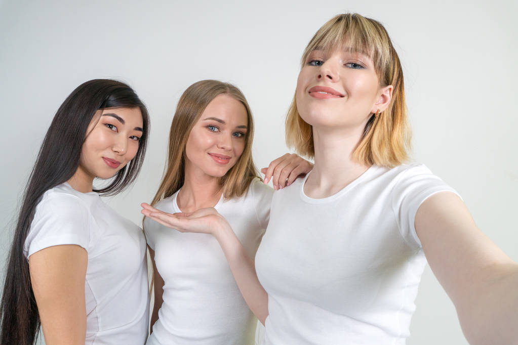 Όμορφη αστεία κορίτσια κάνουν selfie. Κορίτσια στα λευκά μπλουζάκια. - Φωτογραφία, εικόνα