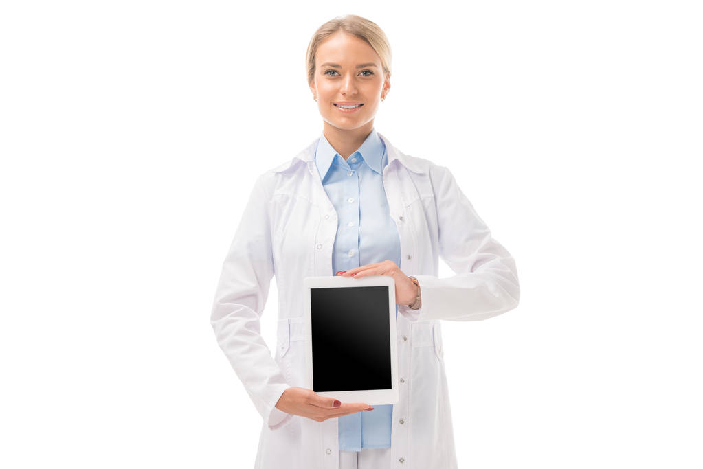 sorridente jovem médico segurando tablet com tela em branco e olhando para a câmera isolada no branco
 - Foto, Imagem