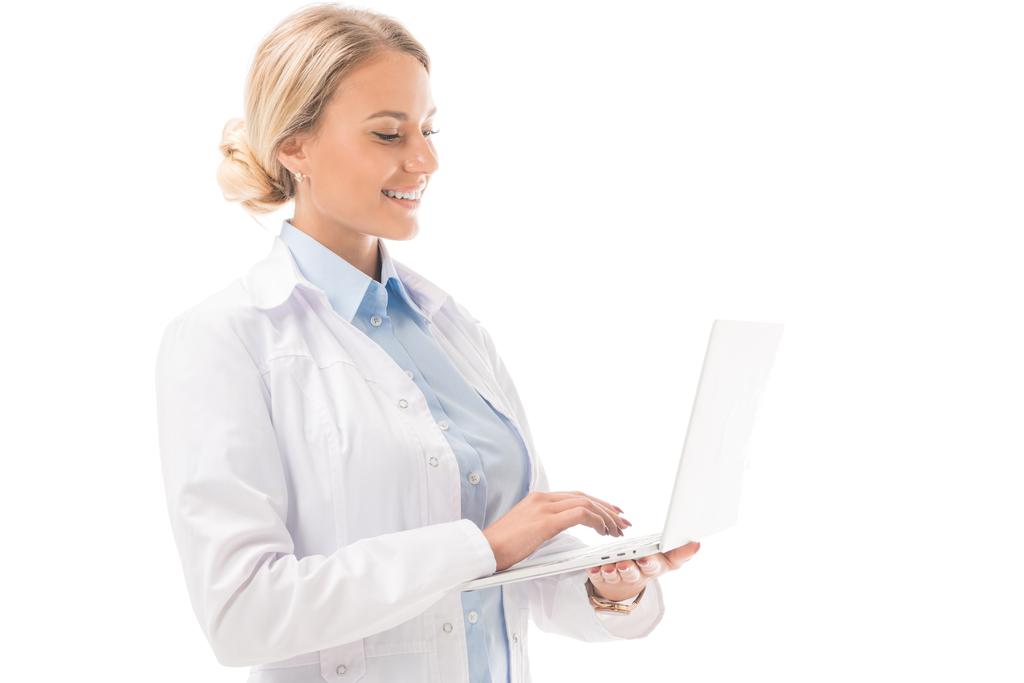 s úsměvem mladá lékařka pracující s přenosným počítačem izolované na bílém - Fotografie, Obrázek