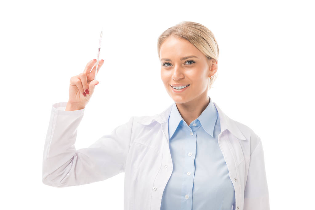 χαμογελαστός νεαρός γιατρός θηλυκό κρατώντας σύριγγα και βλέπουν τα φωτογραφικών μηχανών που απομονώνονται σε λευκό - Φωτογραφία, εικόνα