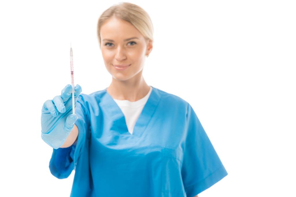 улыбающаяся молодая медсестра, держащая шприц для инъекции и глядя на камеру, изолированную на белом
 - Фото, изображение