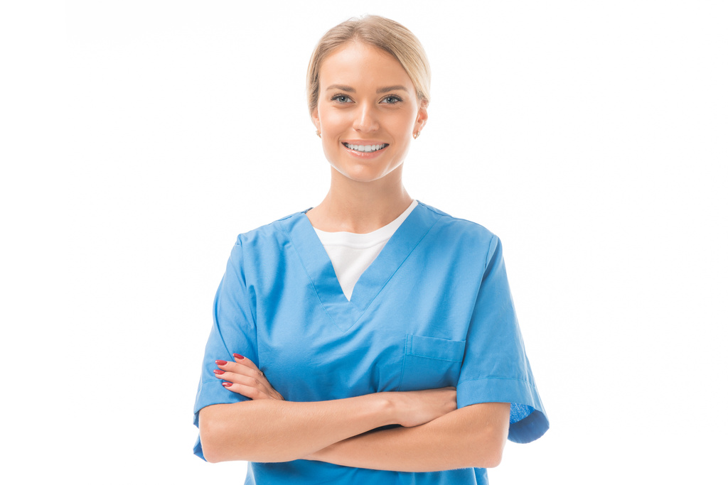 glimlachend jonge verpleegster met gekruiste armen kijken camera geïsoleerd op wit - Foto, afbeelding