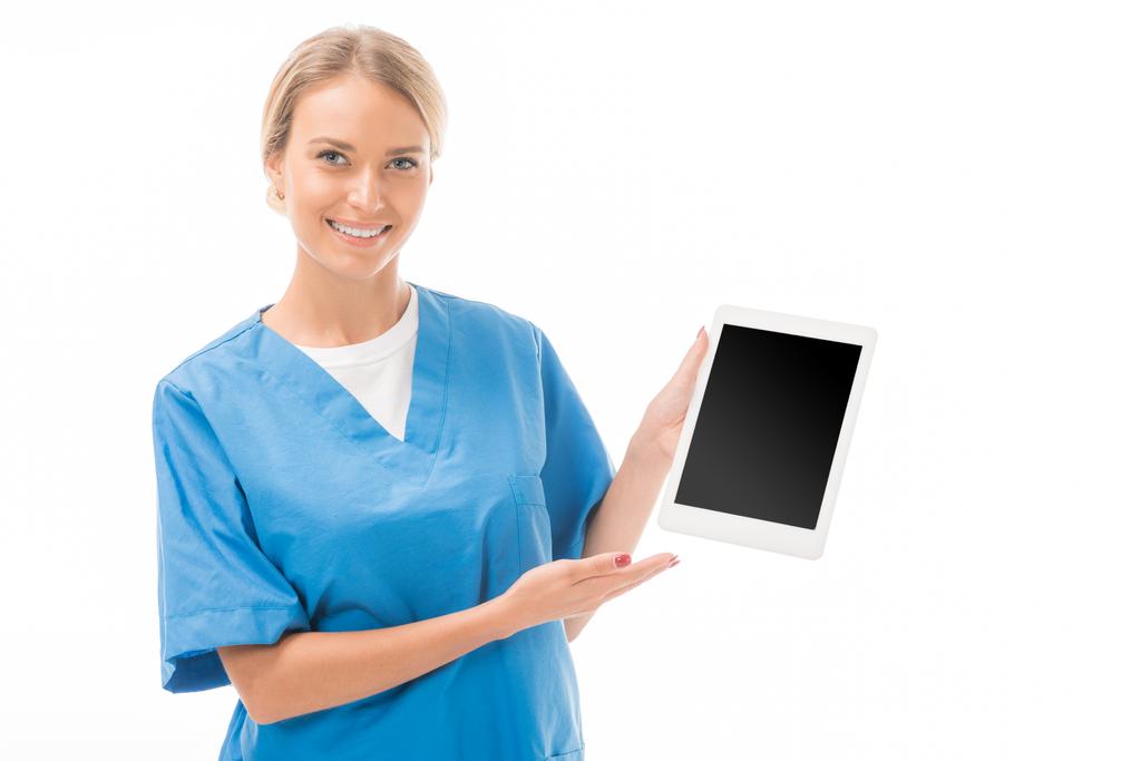 lachende jonge verpleegster wijzend op tablet met leeg scherm geïsoleerd op wit - Foto, afbeelding