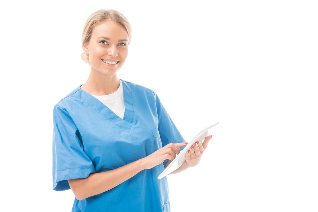 χαρούμενος νεαρός νοσοκόμα λειτουργεί με ψηφιακό tablet και βλέπουν τα φωτογραφικών μηχανών που απομονώνονται σε λευκό - Φωτογραφία, εικόνα
