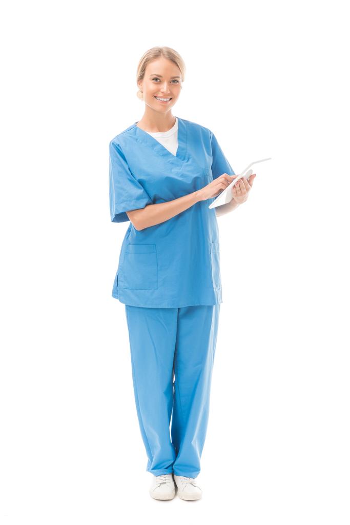uśmiechnięta młoda pielęgniarka praca z cyfrowego tabletu i patrząc na kamery na białym tle - Zdjęcie, obraz