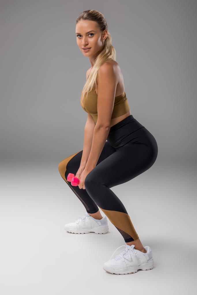 sportiva giovane donna che fa squat con manubri su grigio
 - Foto, immagini