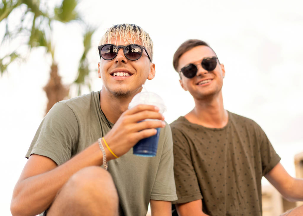 Kaksi miestä juo cocktaileja trooppisella rannalla.
 - Valokuva, kuva