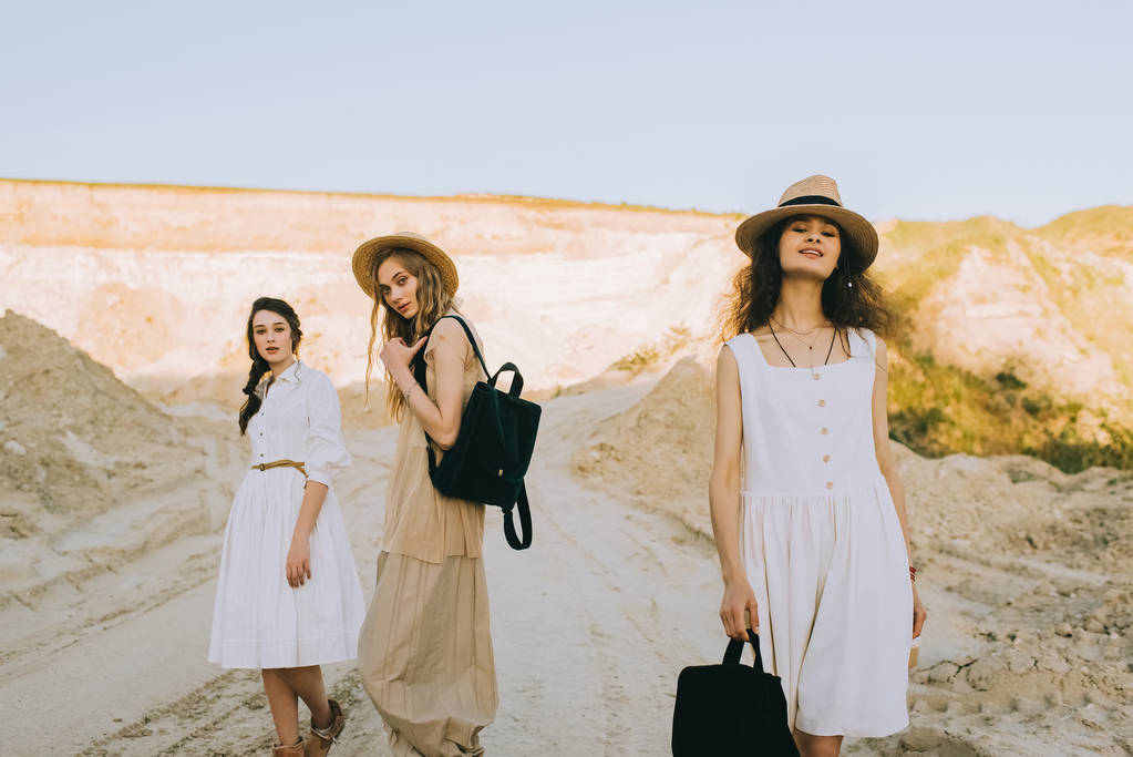 ładne dziewczyny w eleganckie suknie i słomkowe kapelusze, chodzenie z plecakami w piaszczyste Kanion - Zdjęcie, obraz